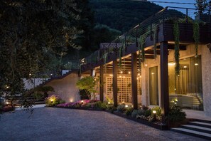A modern building with a staircase leading to a second floor, surrounded by lush greenery and well-lit outdoor areas.