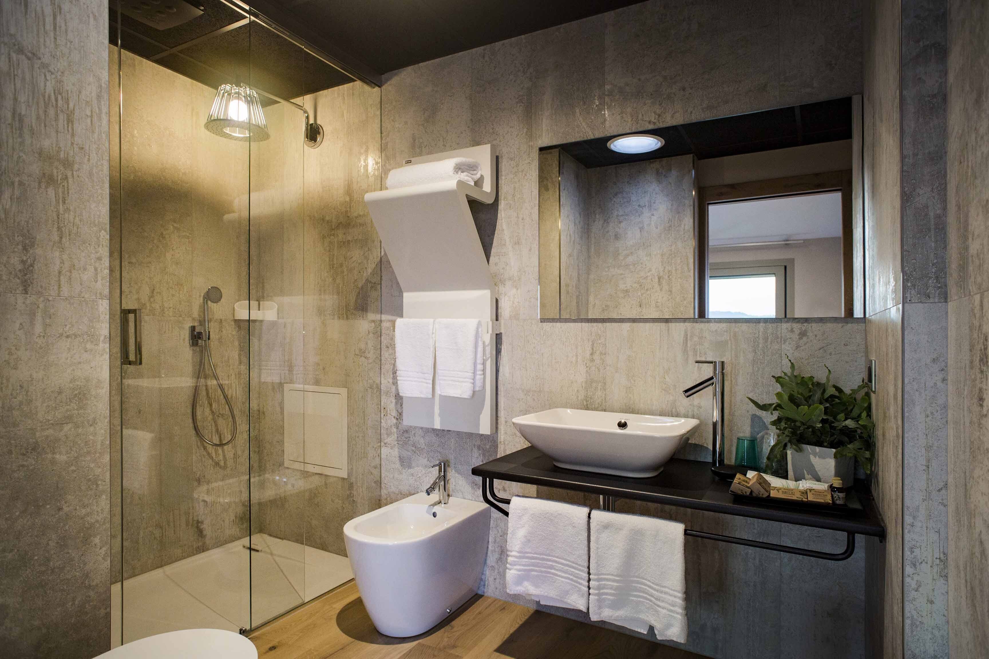 Un baño moderno con ducha de vidrio, un bidé, un lavabo con espejo y un perchero para toallas.