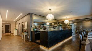 A modern bar area with a dark counter, multiple bottles, and a large mirror. - Ristorante Hotel La Rosina (Marostica)