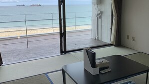 Een kamer met tatami vloeren, een lage tafel en uitzicht op zee met schepen.