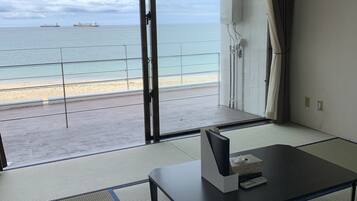 A room with tatami flooring, a low table, and a view of the sea with ships.