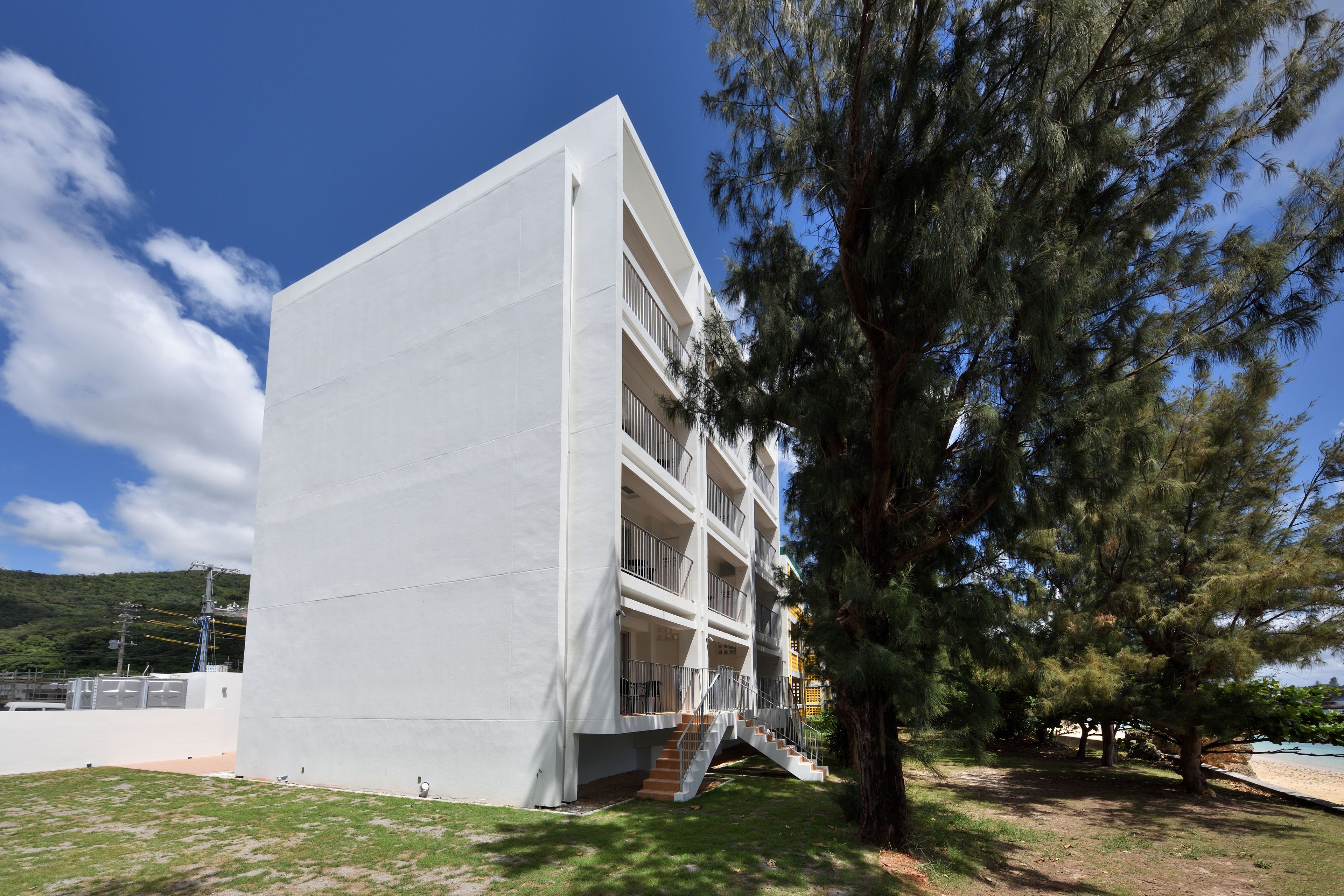A modern building with a white facade, multiple balconies, and a staircase leading to the entrance.