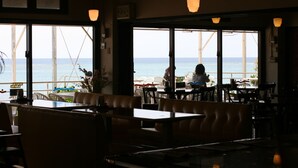 Een interieur van een restaurant met grote ramen met uitzicht op zee, met tafels en stoelen klaar voor diners.
