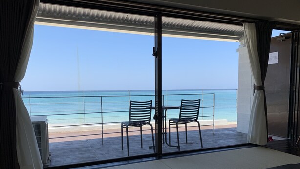 Een balkon met twee stoelen en een tafel, met uitzicht op een strand en de oceaan.