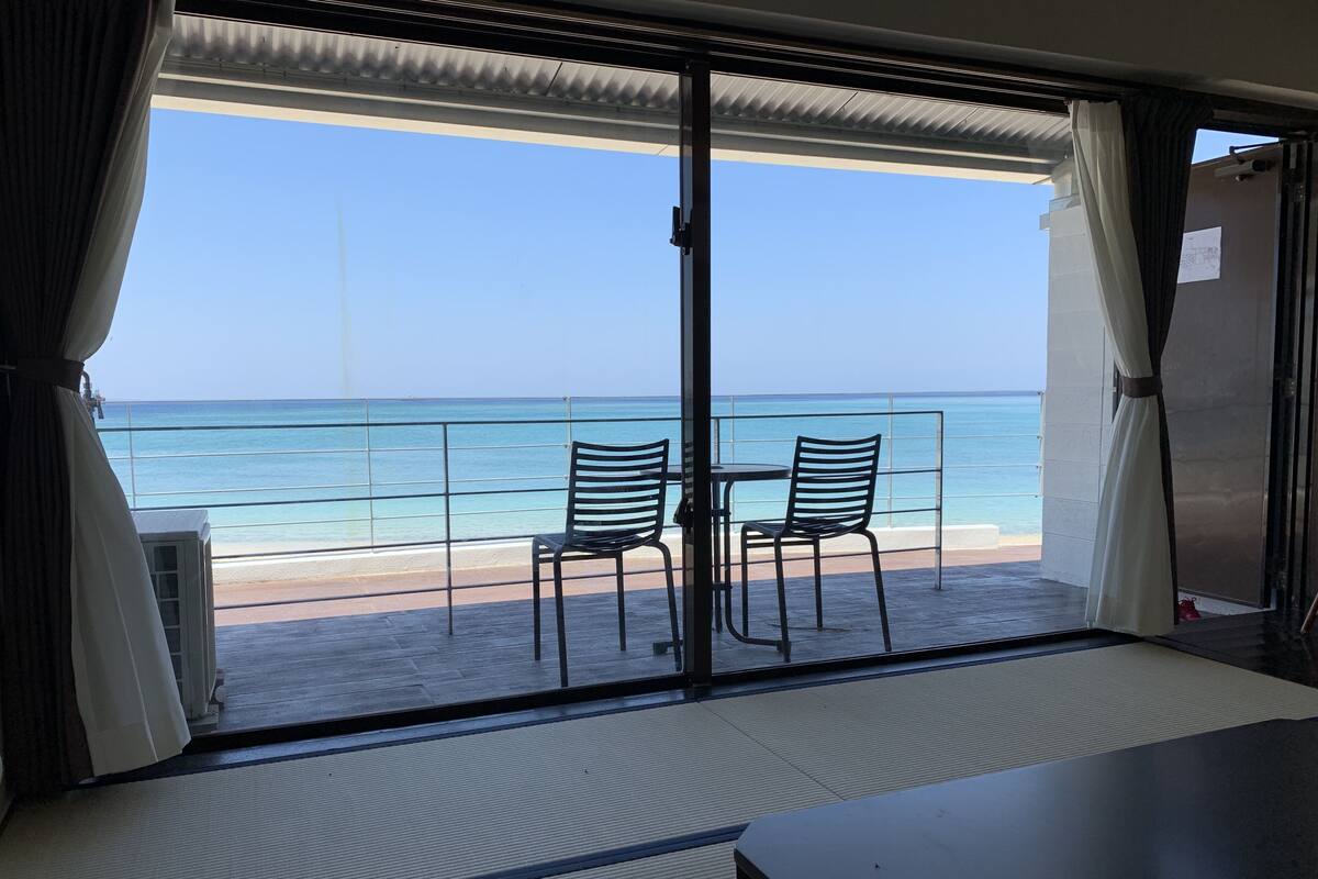 A balcony with two chairs and a table, overlooking a beach and the ocean.