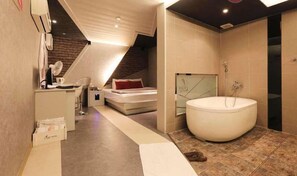 A modern bedroom with a sloped ceiling, a large bathtub, and a separate sleeping area. - Foxy Motel (Busan)