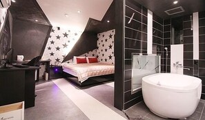 A modern bedroom with a sloped ceiling, a bed with a star-patterned headboard, a large white bathtub, and a walk-in closet. - Foxy Motel (Busan)