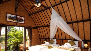 Una habitación con dos camas, ventilador de techo y vistas al verde exterior.