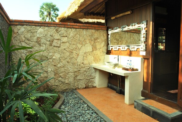 Un baño con pared de piedra, lavabo, espejo y techo de paja.