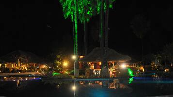 A nighttime resort with a pool, palm trees, and illuminated buildings.