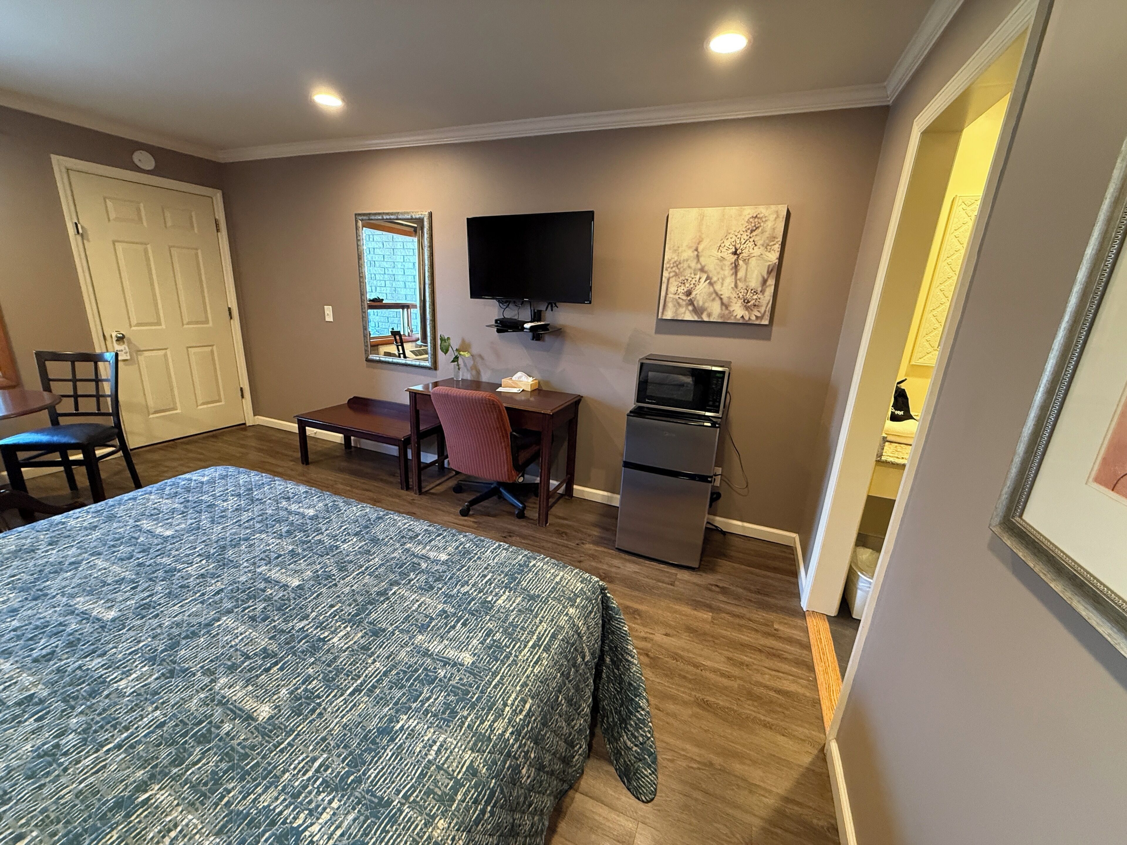 A compact hotel room with a bed, desk, chair, TV, and refrigerator.