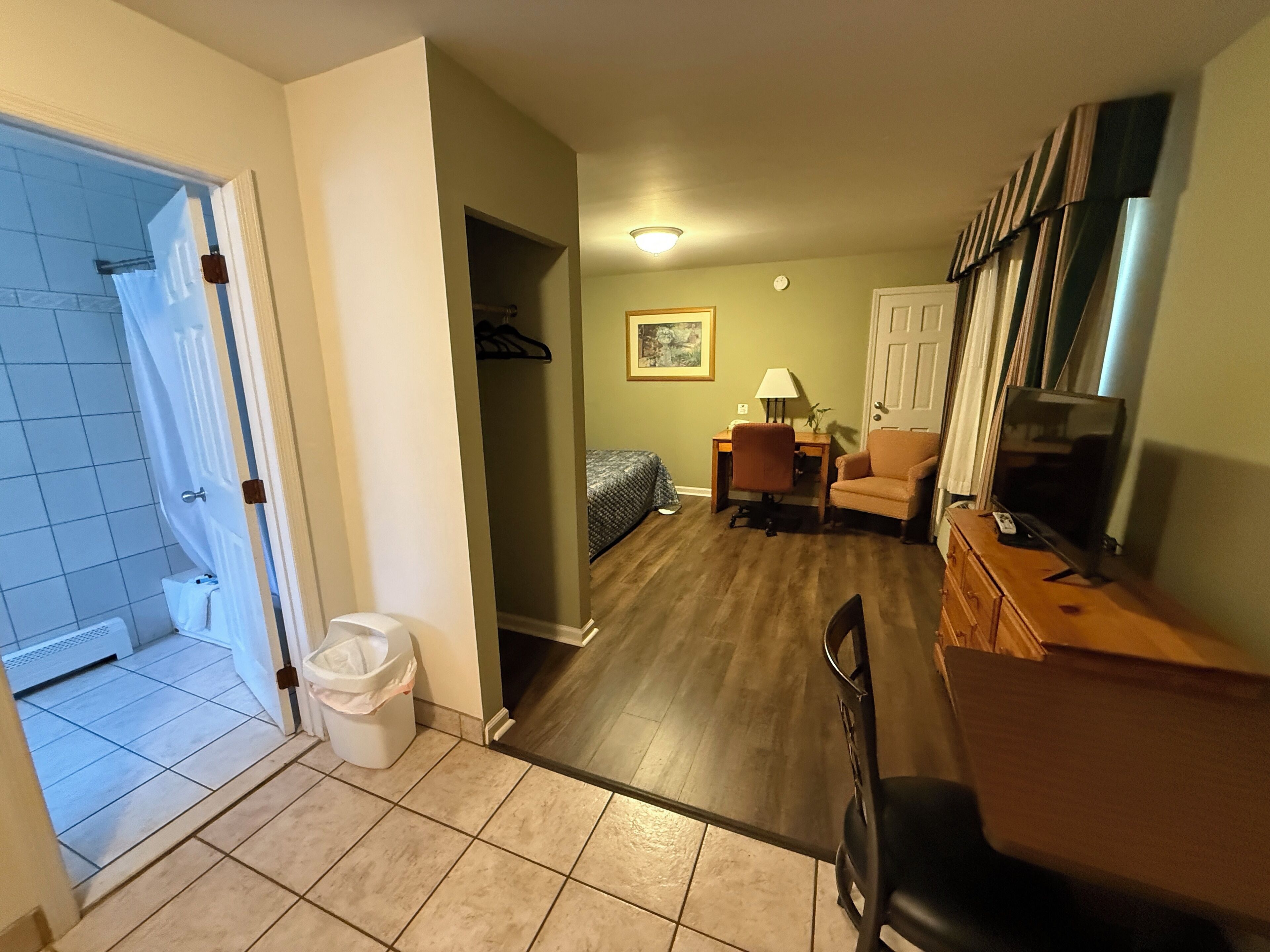 Un espacio habitable compacto con ducha, un escritorio pequeño, una silla, un sofá y un televisor.