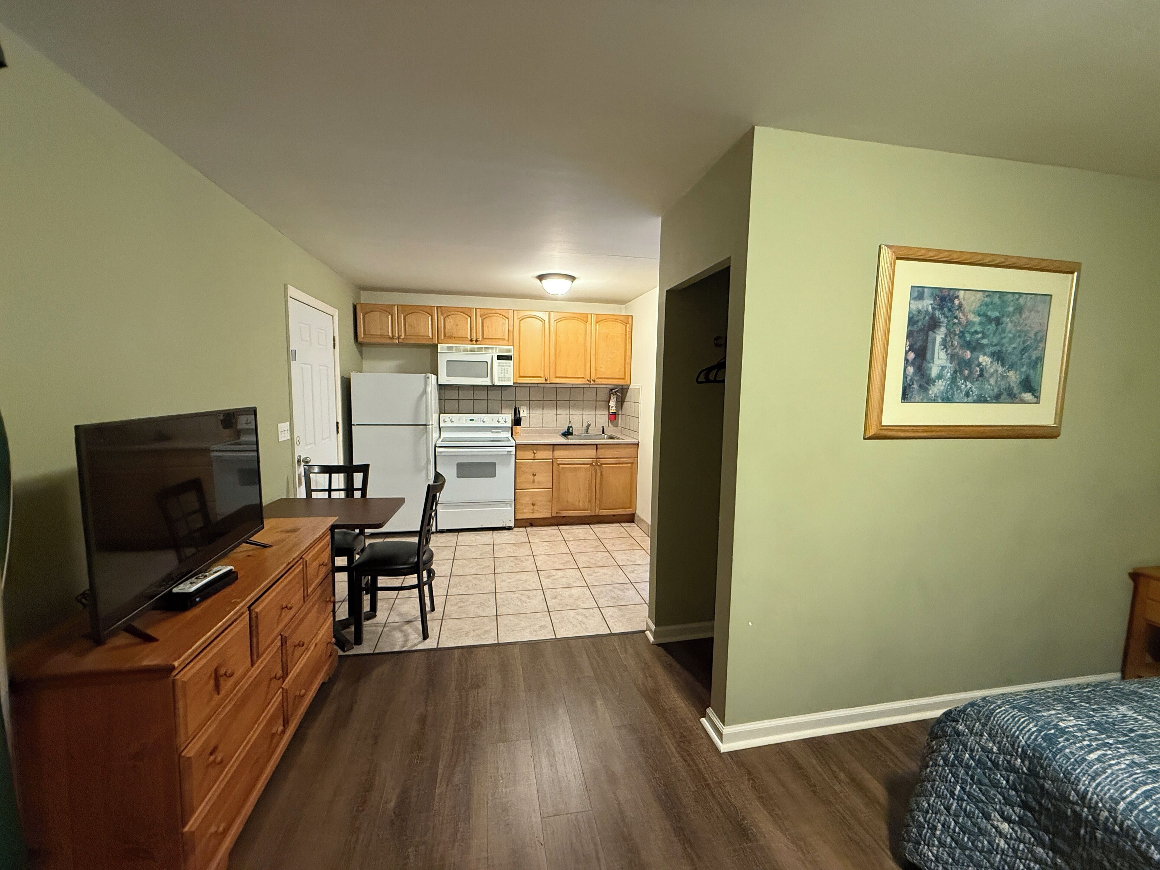 A compact kitchen with wooden cabinets, a microwave, and a refrigerator. There is a dining area with a table and chairs.