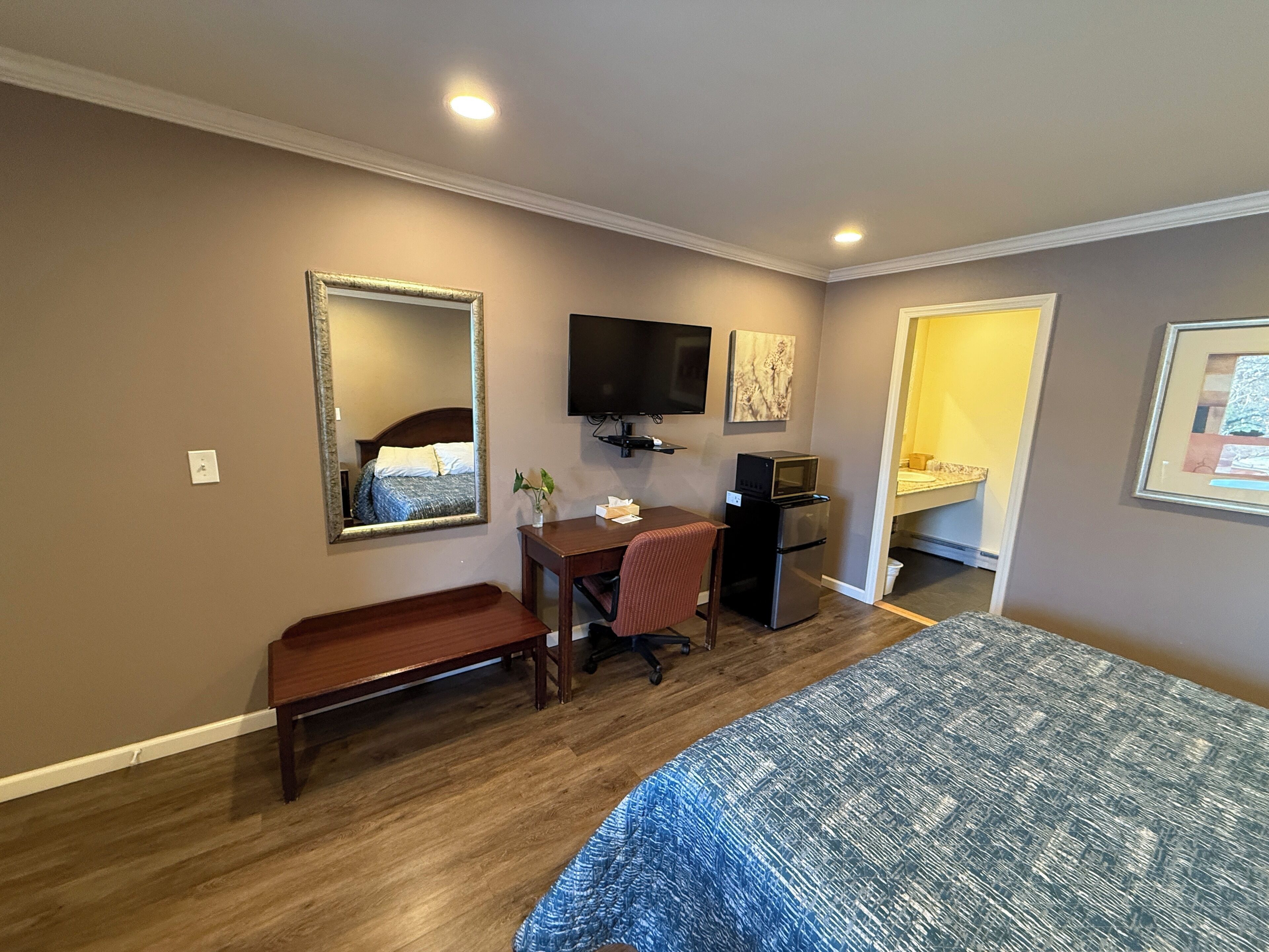 A hotel room with a bed, a desk with a chair, a television, a microwave, and a refrigerator.