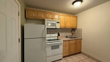 Cocina compacta con refrigerador, estufa, microondas y gabinetes de madera.