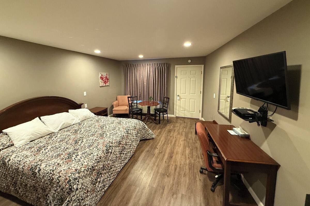 A hotel room with a bed, a desk, a chair, a television, and a door.