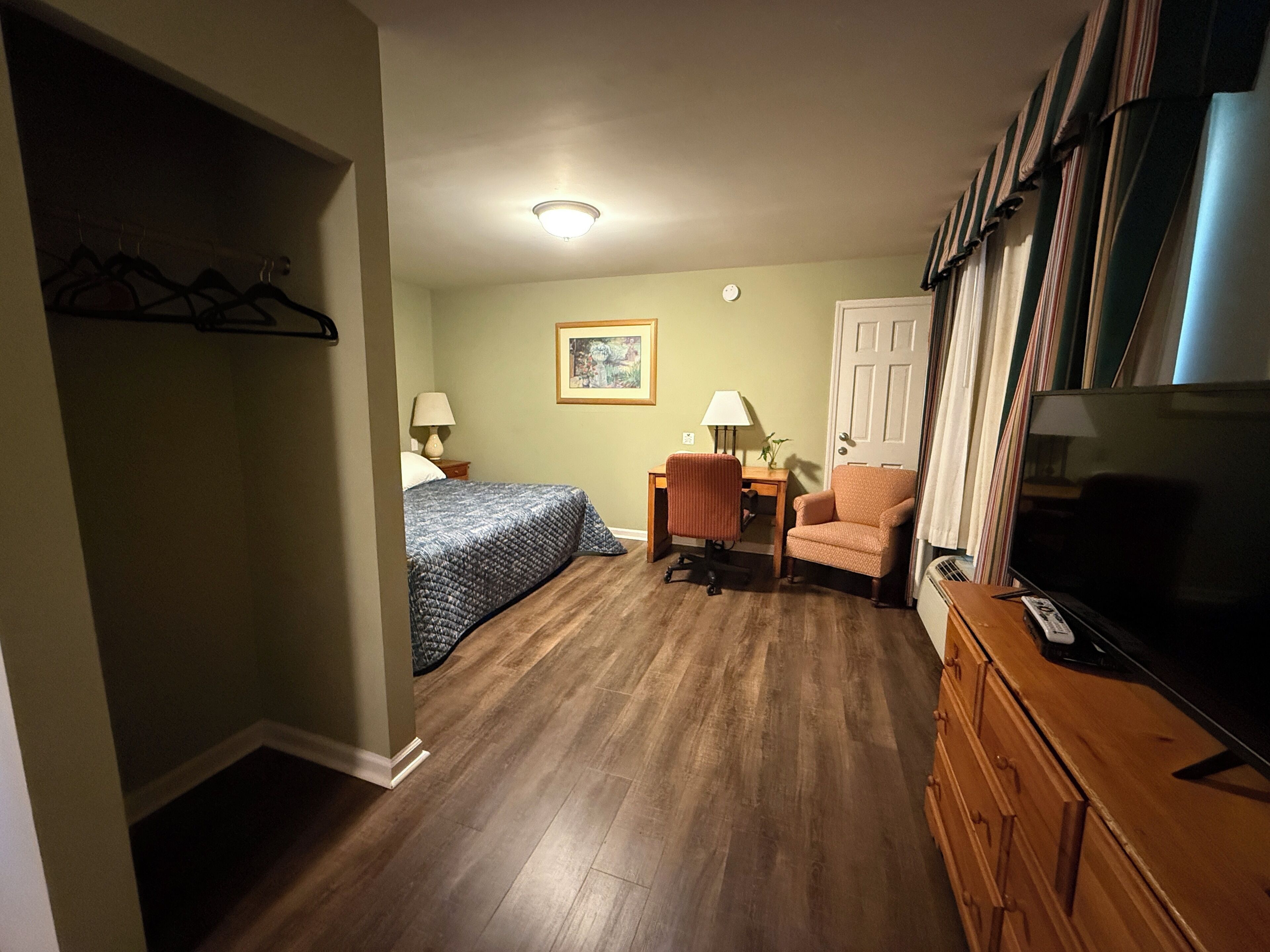 A compact hotel room with a bed, a desk, a chair, a television, and a wardrobe.