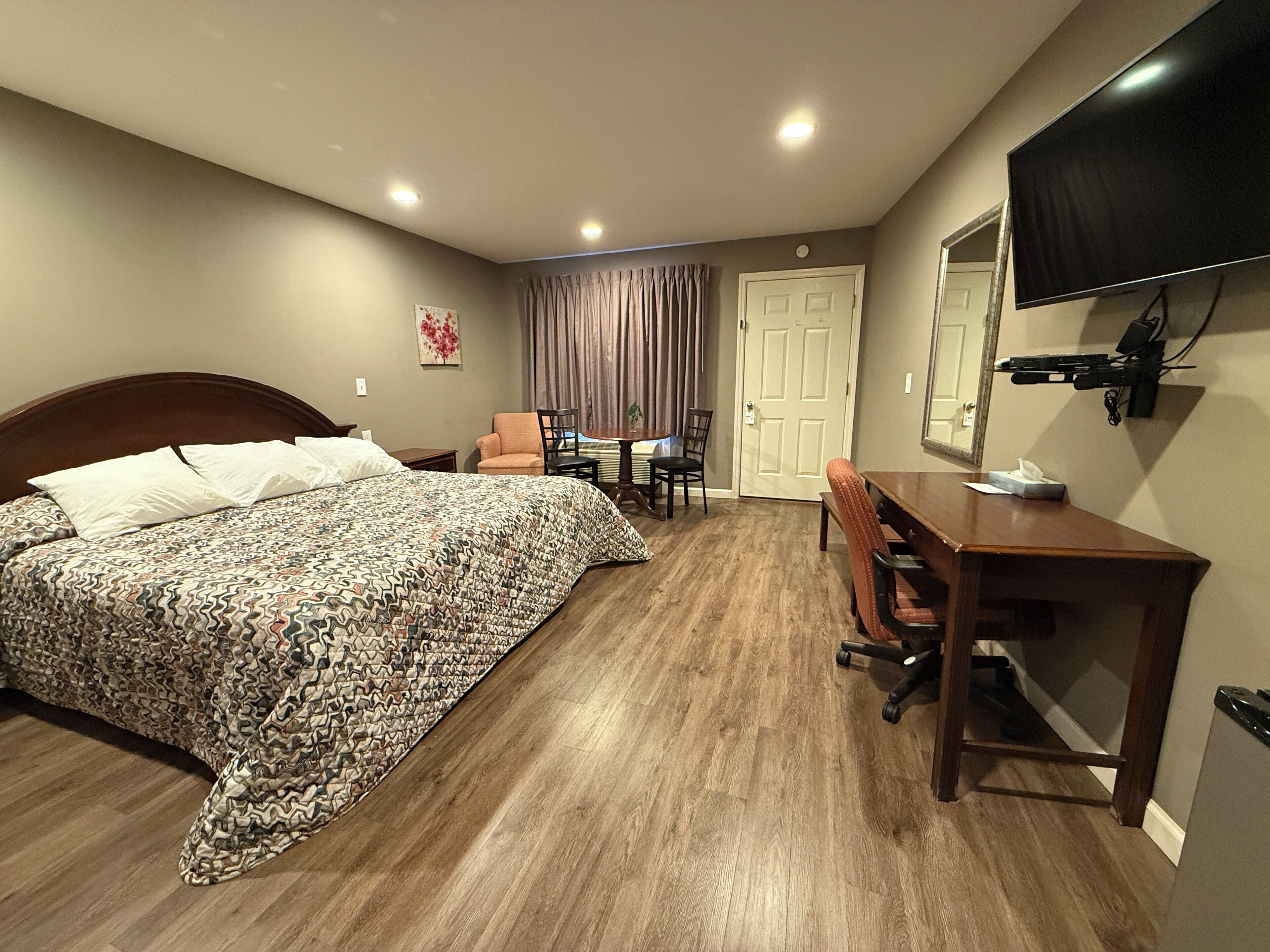Una habitación de hotel con una cama, un escritorio, una silla, un televisor y una puerta.