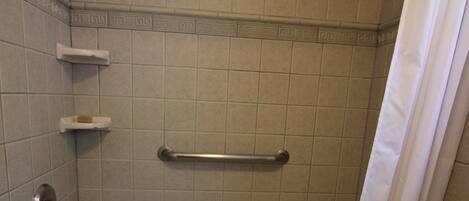 Un baño de hotel estándar con bañera, cortina de ducha, barandilla y jabonera.