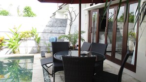 Un patio con mobiliario de mimbre, una mesa de vidrio y un paraguas rojo.