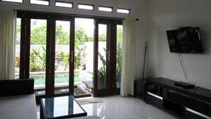 Una sala de estar con televisor, una mesa de vidrio y un ventanal corredera que da a un jardín.