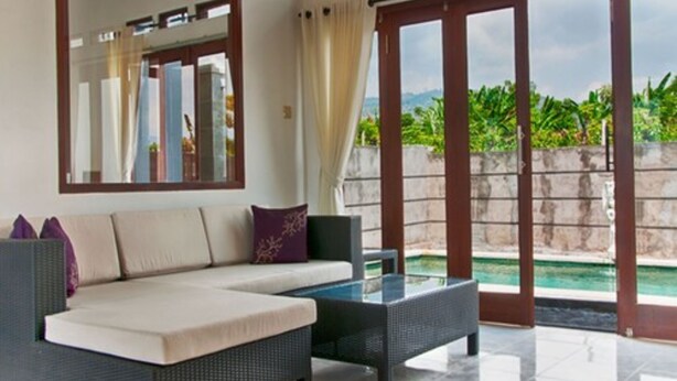 Una sala de estar moderna con un sofá, una mesa de centro de vidrio y un amplio ventanal corredero que da a una zona de piscina.