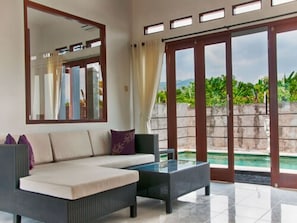Una sala de estar moderna con un sofá, una mesa de centro de vidrio y un amplio ventanal corredero que da a una zona de piscina.