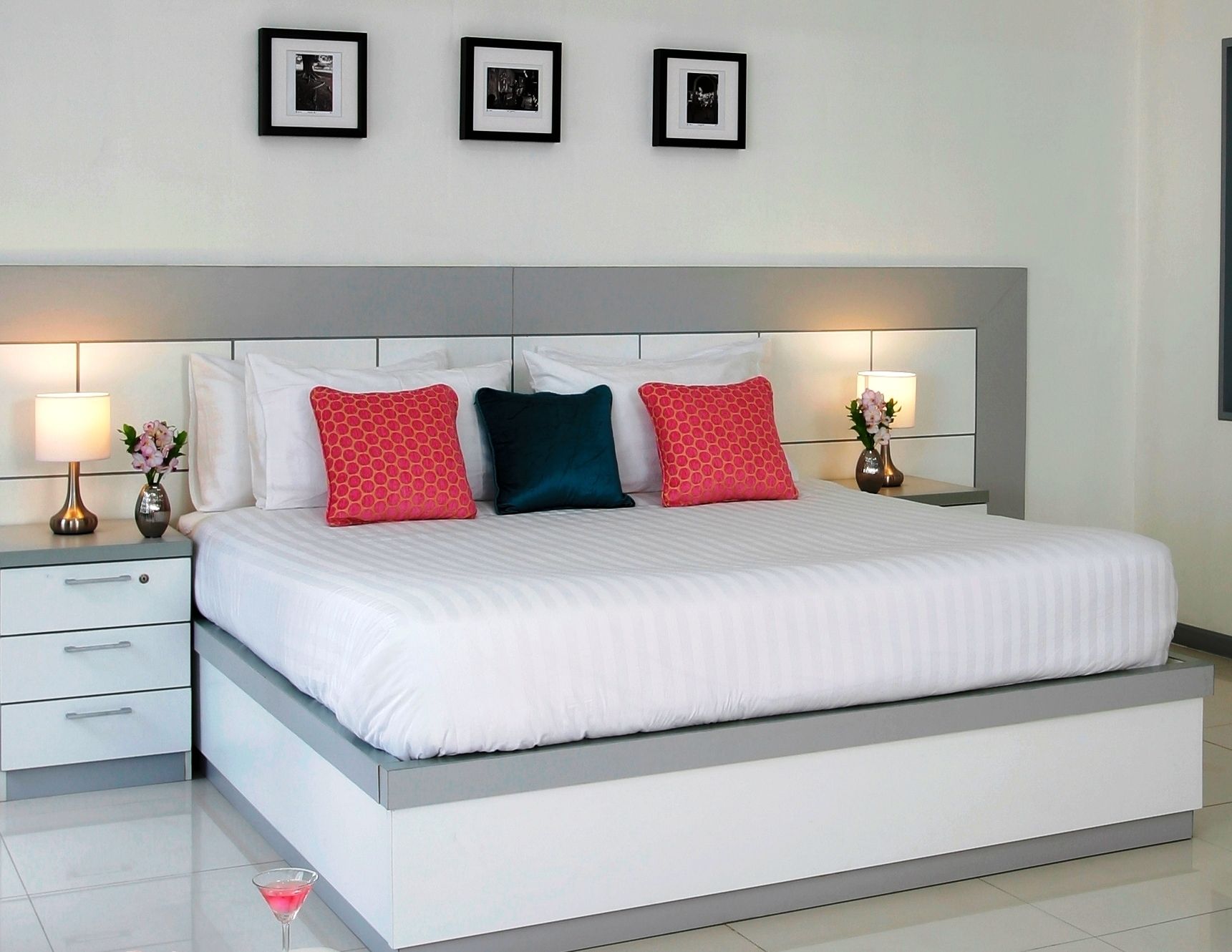 A modern hotel room with a large bed, white bedding, and three framed pictures on the wall.
