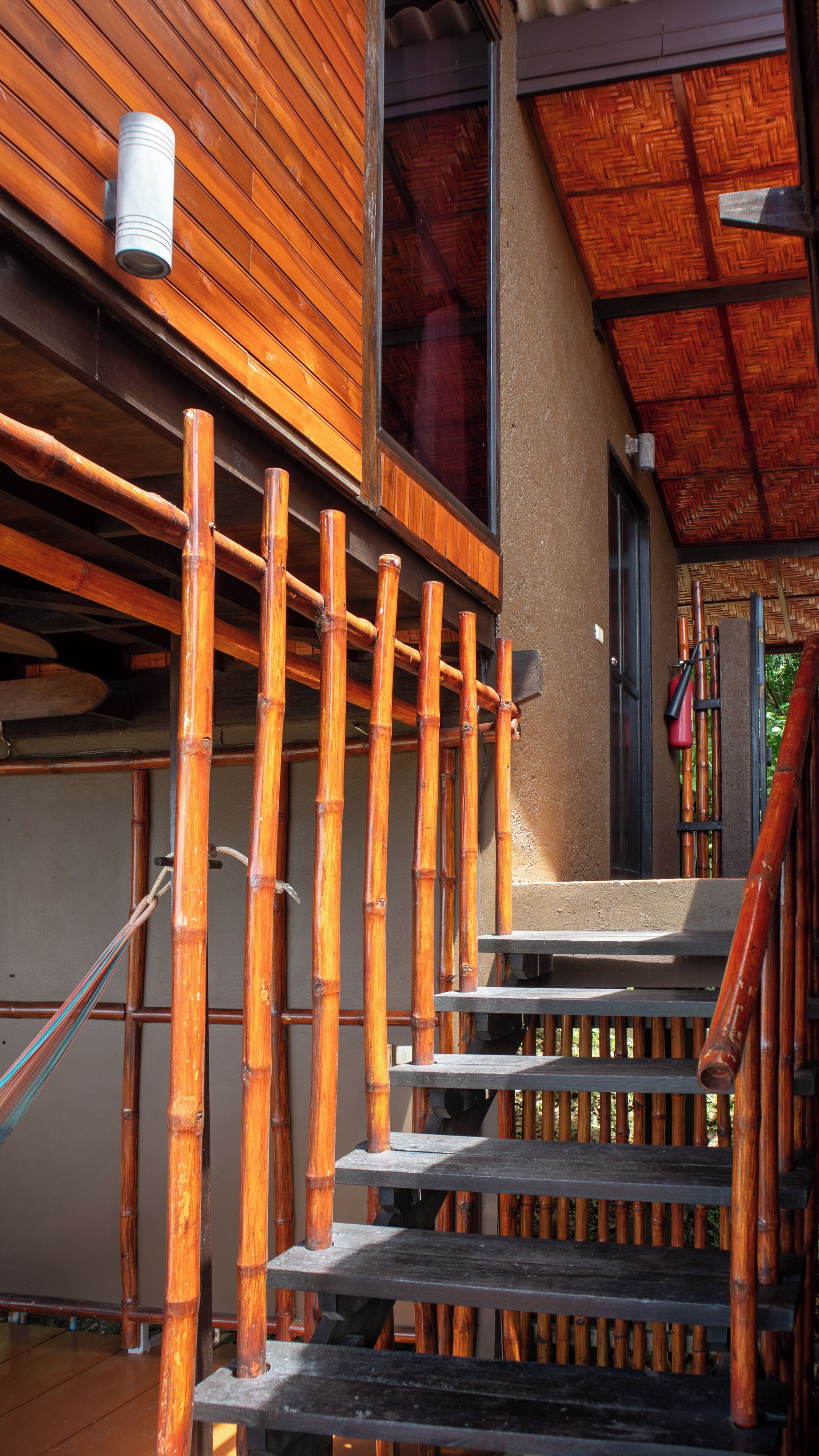 Un escalier en bois avec une rampe en bambou, menant à un espace d’entrée abrité.