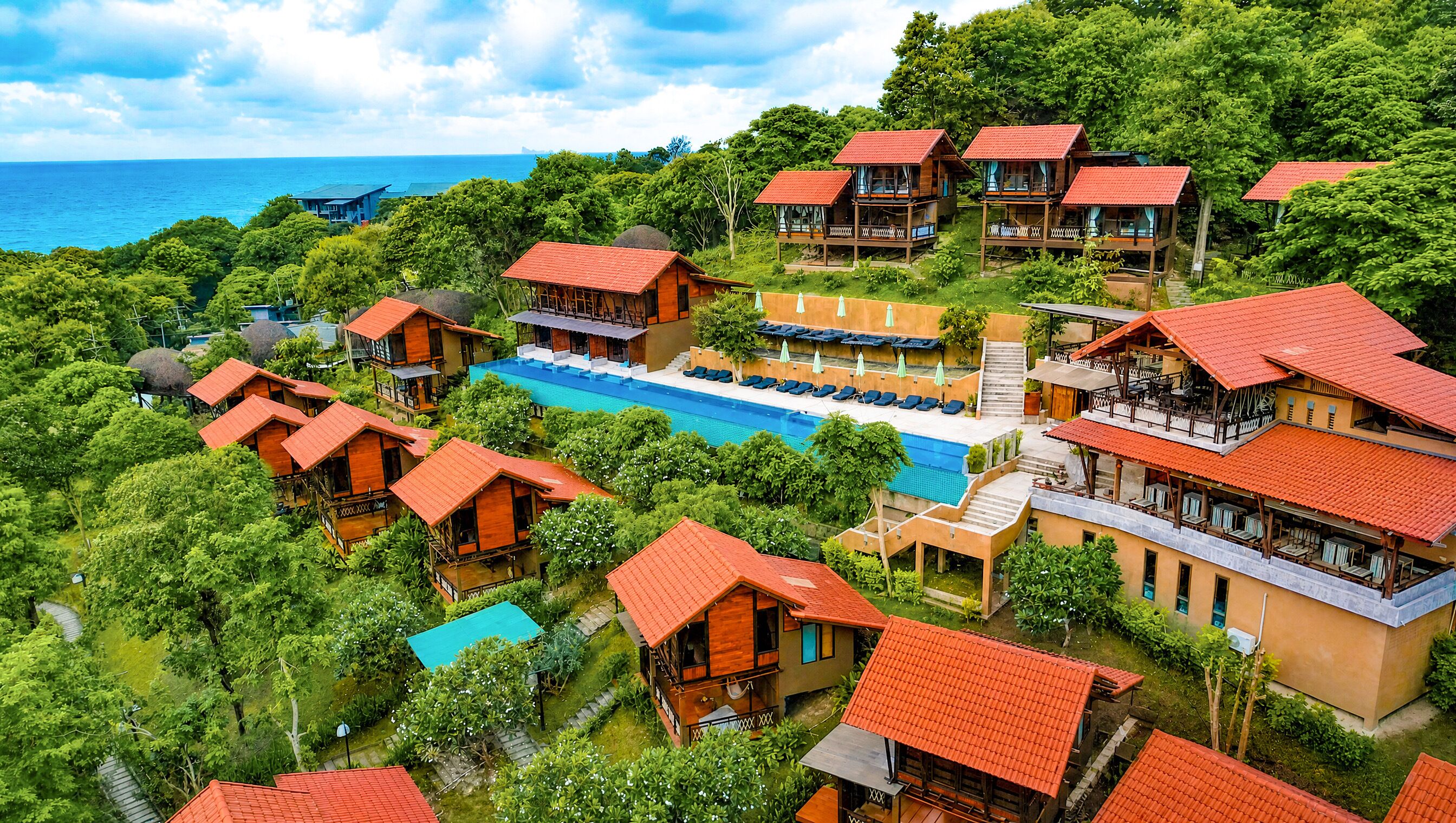 A resort with multiple wooden buildings, a central swimming pool, and a view of the ocean.