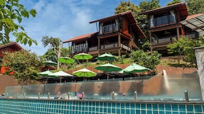 A hotel with multiple balconies, a swimming pool, and green umbrellas.