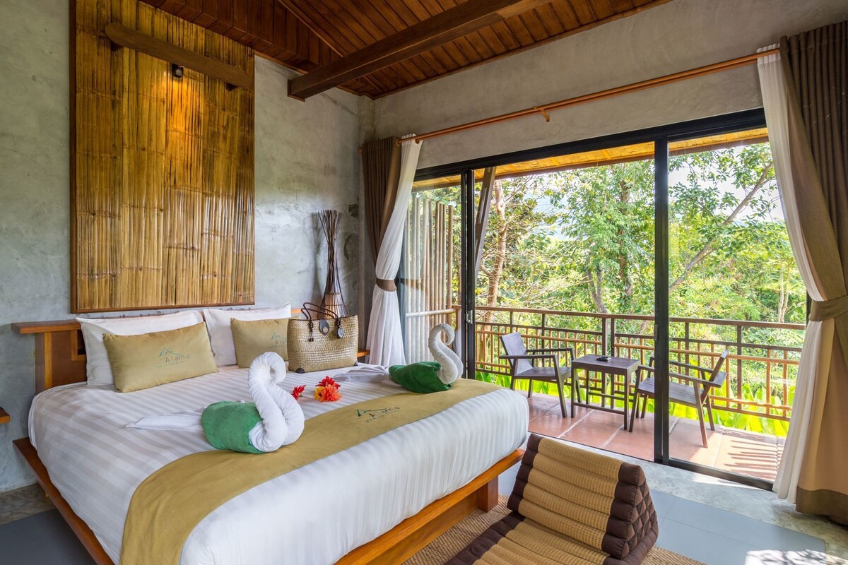 A bedroom with a bed, pillows, a swan-shaped pillow, a woven basket, and a balcony with chairs and a table.