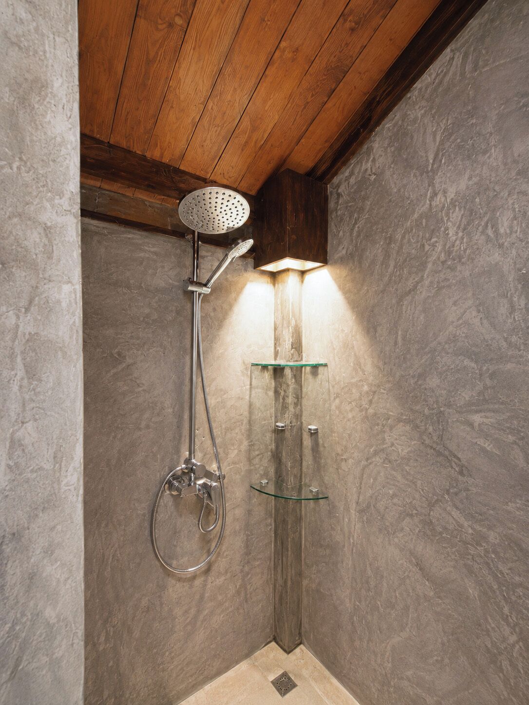 A shower with a handheld showerhead and a glass shelf unit.