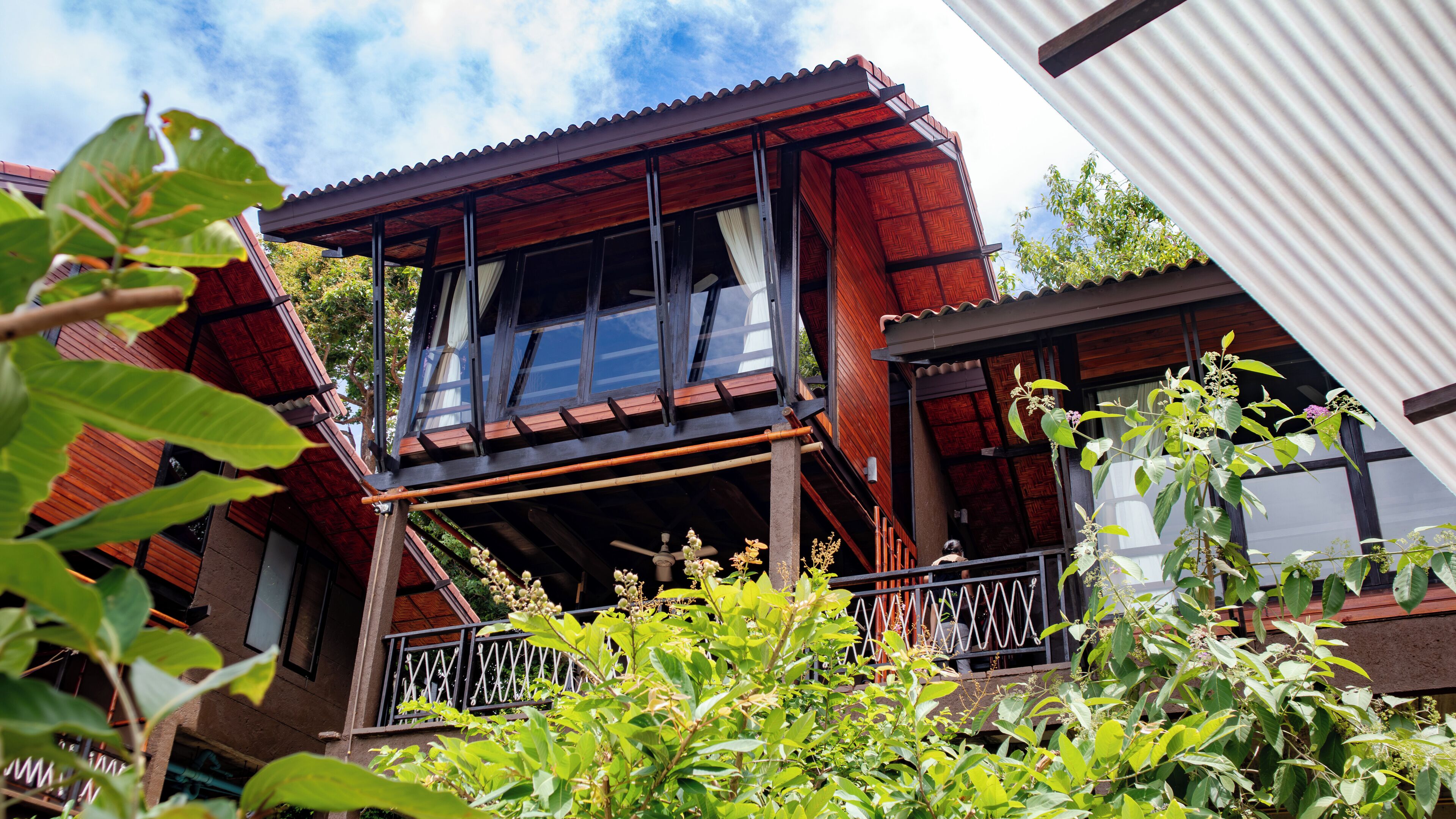 Uma casa de madeira de dois andares com varanda, janelas amplas e um ventilador de teto à vista.