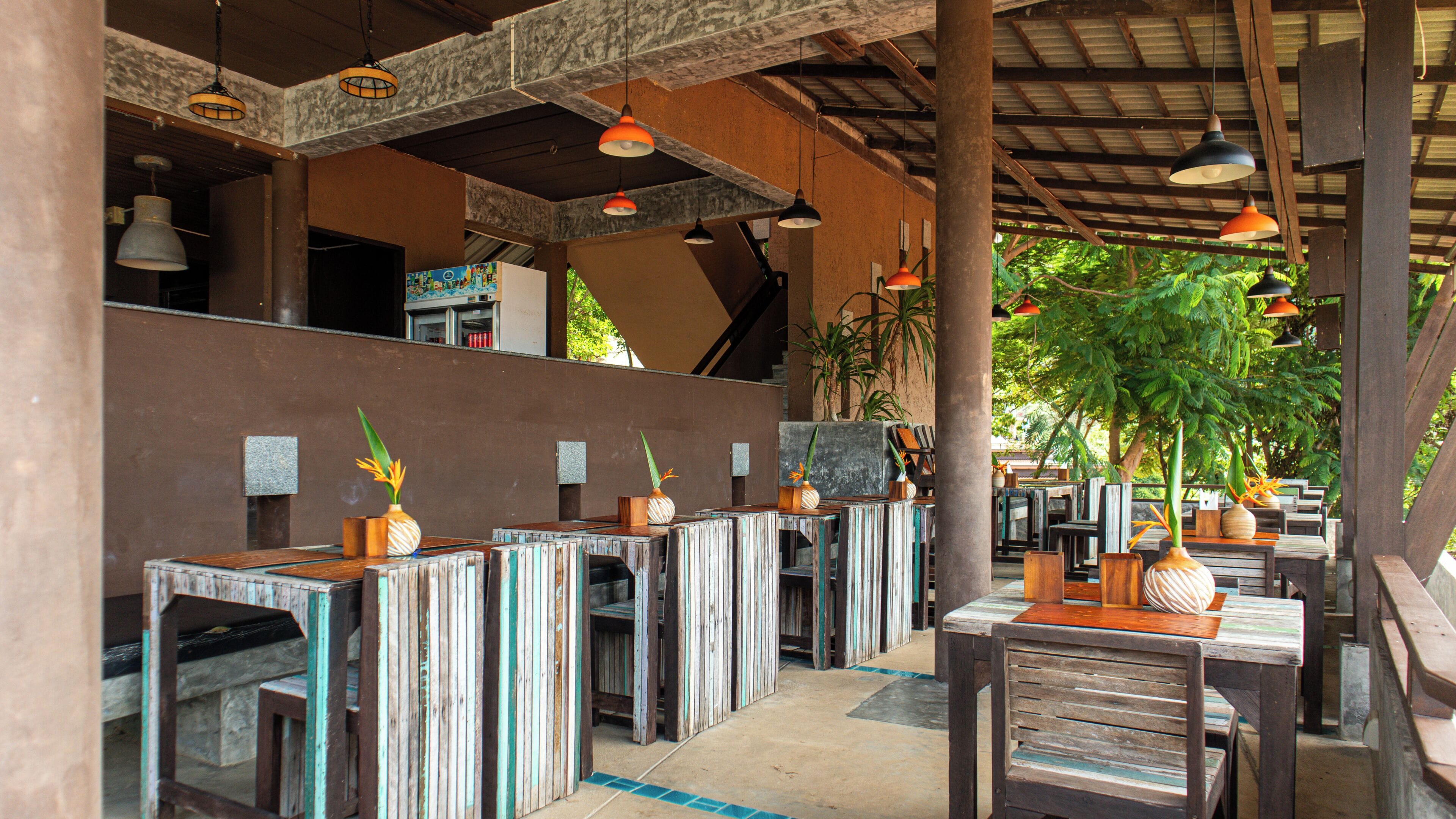 Un restaurante con mesas y sillas de madera, lámparas colgantes y plantas en macetas.