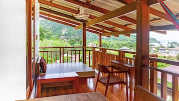 Una terraza de madera con mesa y sillas, con vistas a un paisaje verde y exuberante con casas.