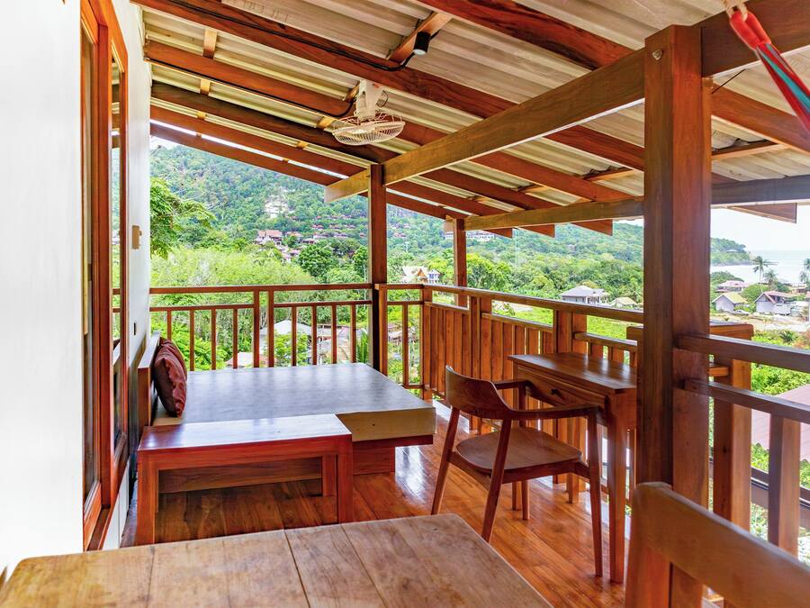 A wooden deck with a table and chairs, overlooking a lush green landscape with houses.