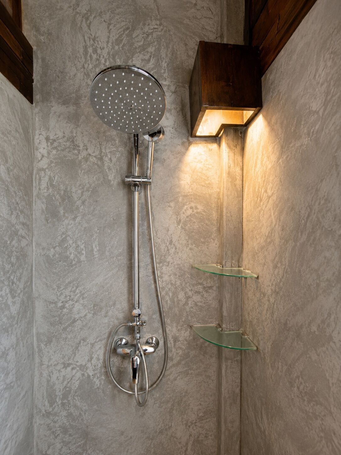 A shower with a handheld showerhead and a wall-mounted light fixture.
