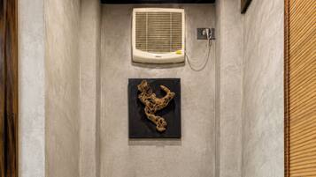 Un baño con inodoro blanco, ducha y aire acondicionado instalado en la pared.