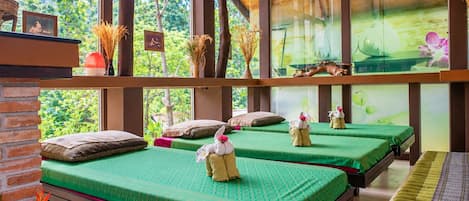 Une chambre avec trois lits, chacun recouvert d’une couverture verte et agrémenté d’oreillers, et une fenêtre donnant sur un paysage verdoyant.