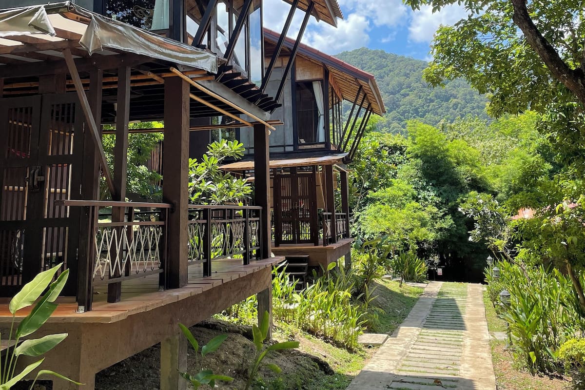 A wooden structure with a balcony, surrounded by lush greenery and a clear sky.
