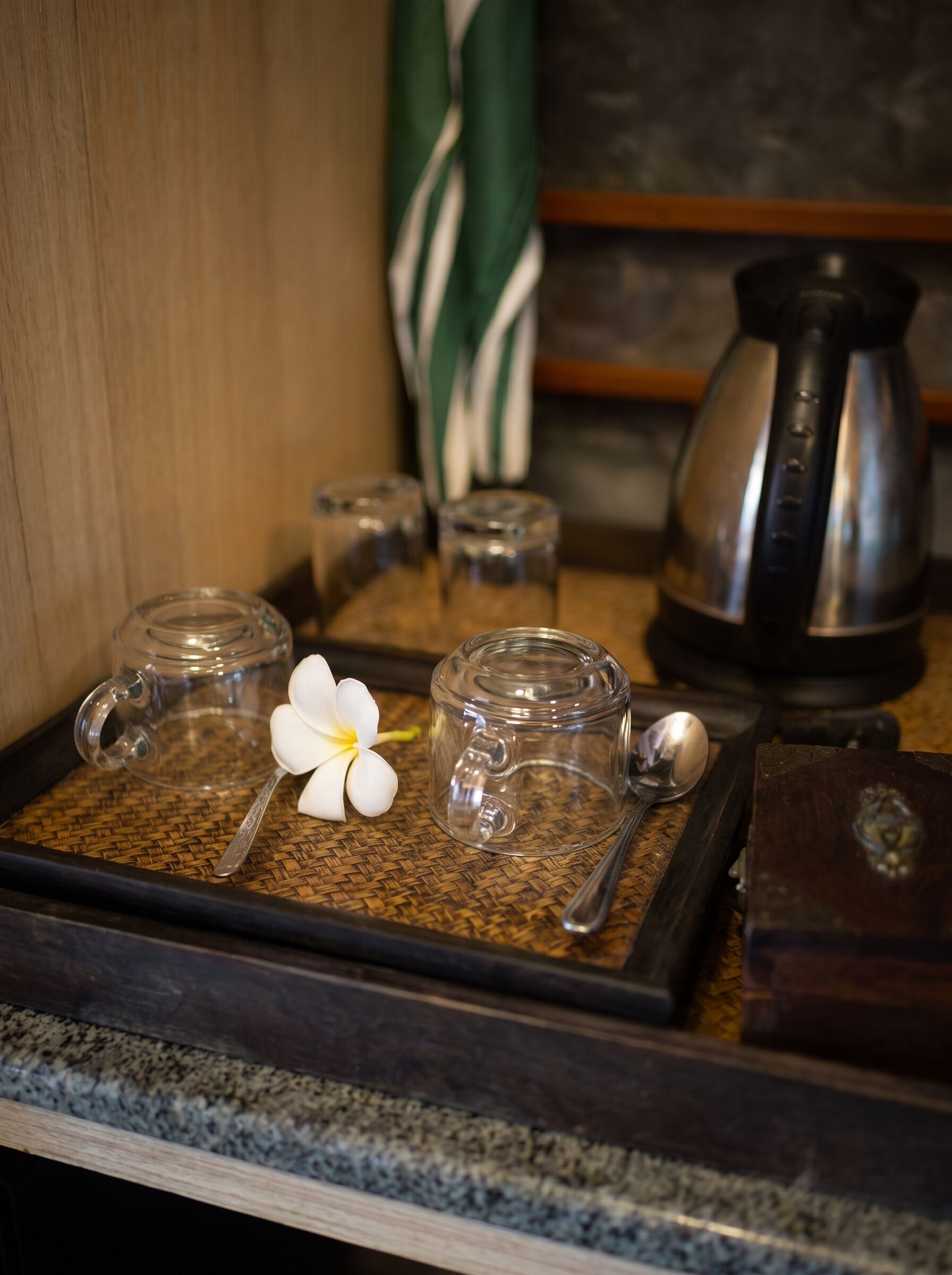 A tray with glass containers, a spoon, and a white flower on a woven mat.
