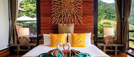 A hotel room with a bed, pillows, a wall art piece, and a view of the outdoors.
