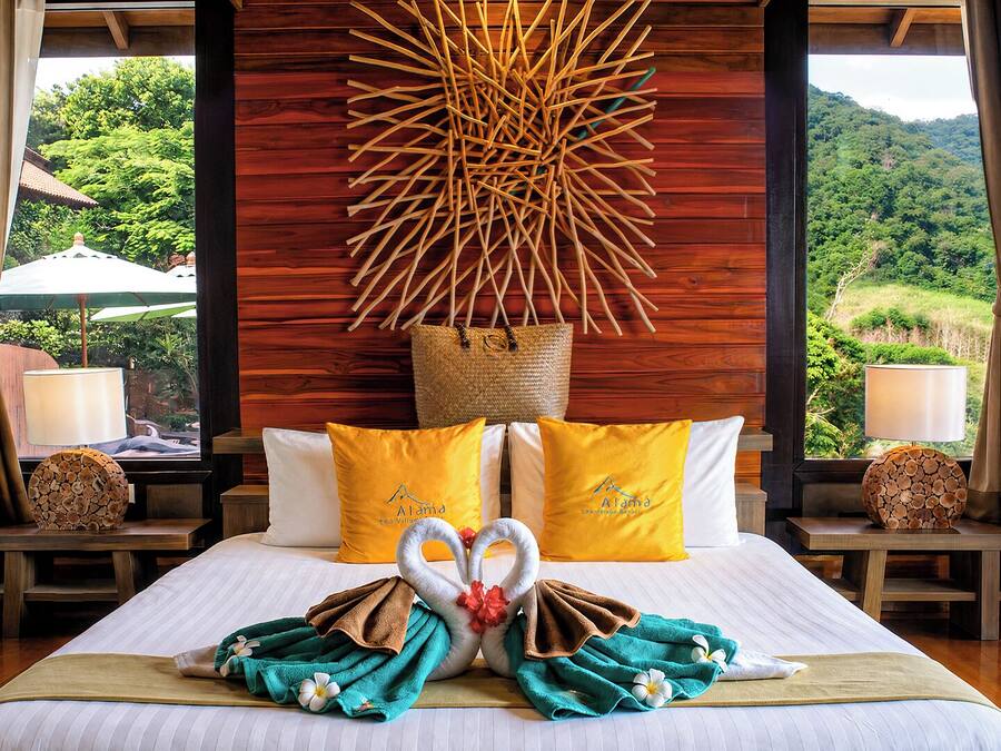 A hotel room with a bed, pillows, a wall art piece, and a view of the outdoors.