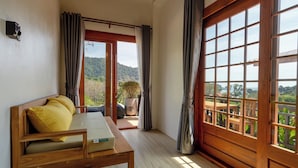 A room with a wooden bed, a small table, and a view of a balcony with a wooden railing and greenery. - Alama Sea Village Resort (Ko Lanta)