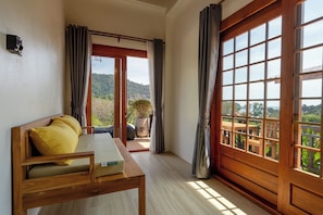 A room with a wooden bed, a small table, and a view of a balcony with a wooden railing and greenery. - Alama Sea Village Resort (Ko Lanta)