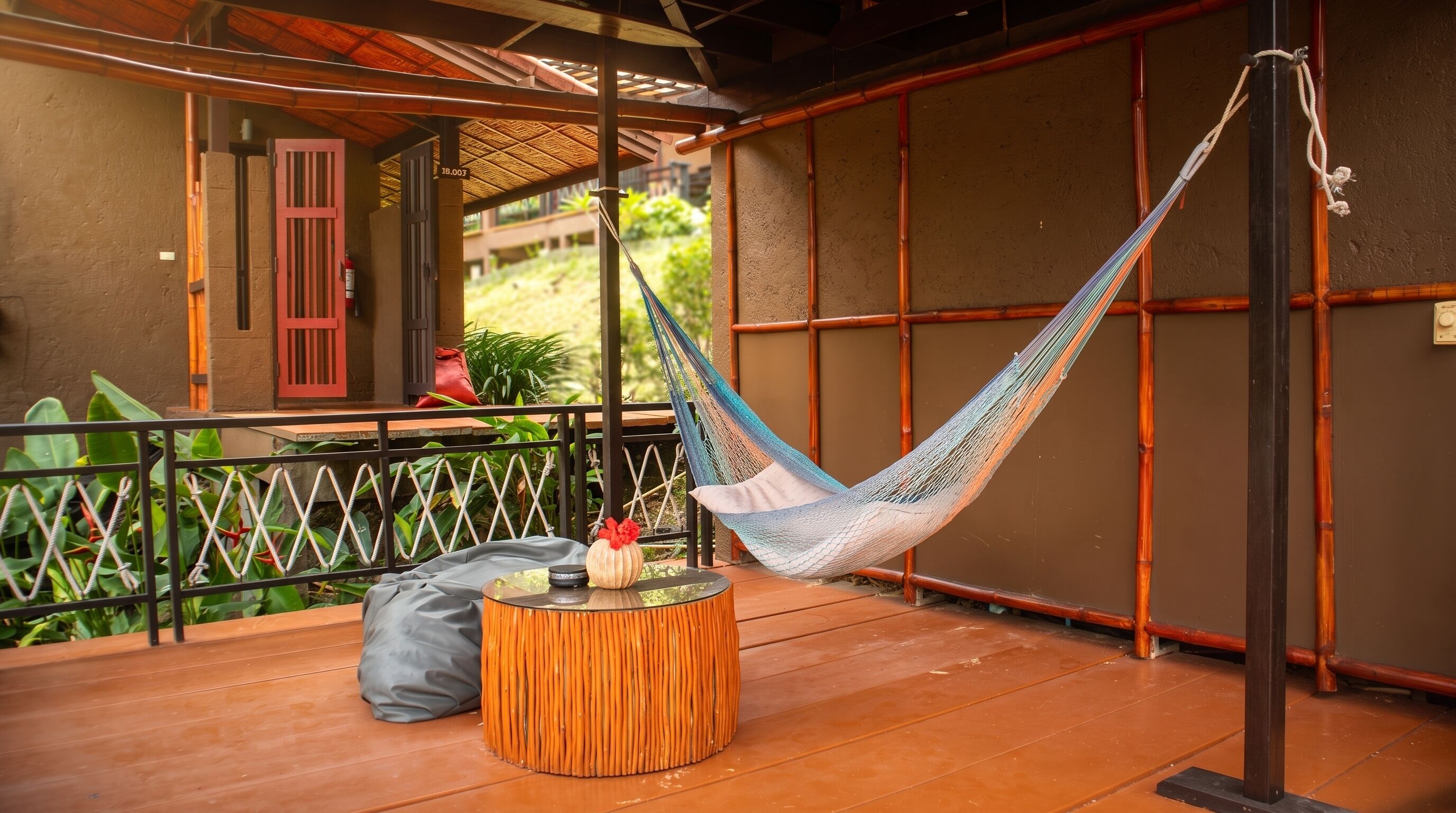 A hammock on a wooden deck with a round table and a red door in the background.