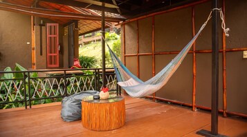 Una hamaca sobre una terraza de madera, con una mesa redonda y una puerta roja al fondo.