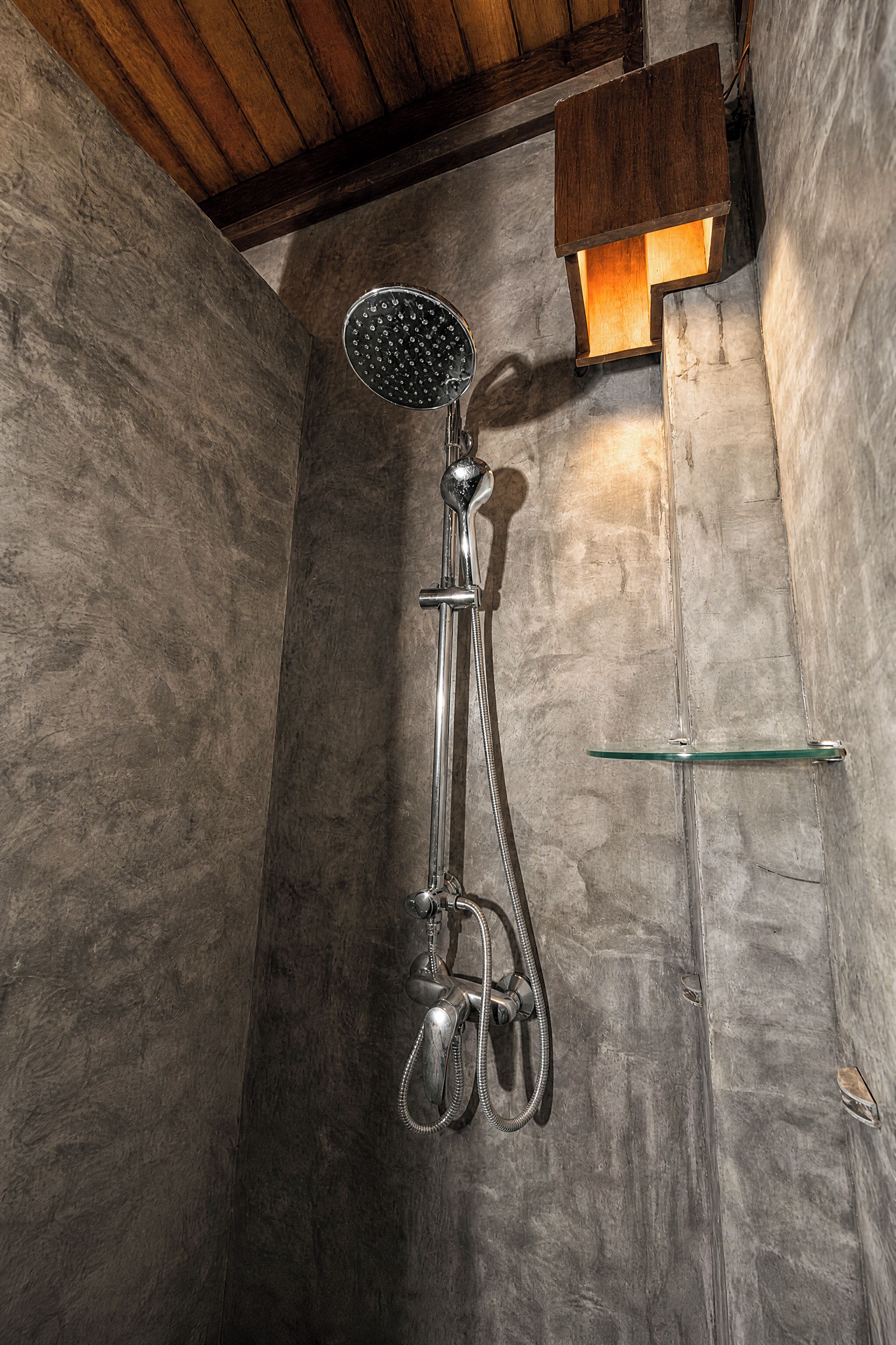 A shower with a handheld showerhead, a glass shelf, and a wooden ceiling.