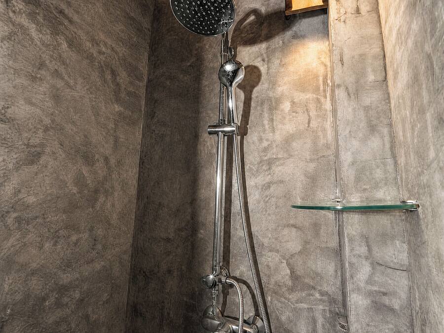 A shower with a handheld showerhead, a glass shelf, and a wooden ceiling.